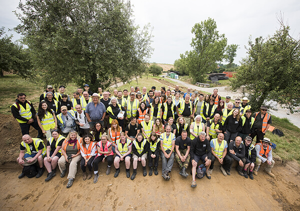 Group shot of the entire 2019 excavation team, posing in the orchard of Mont Saint Jean in Belgium, wearing high vis jackets